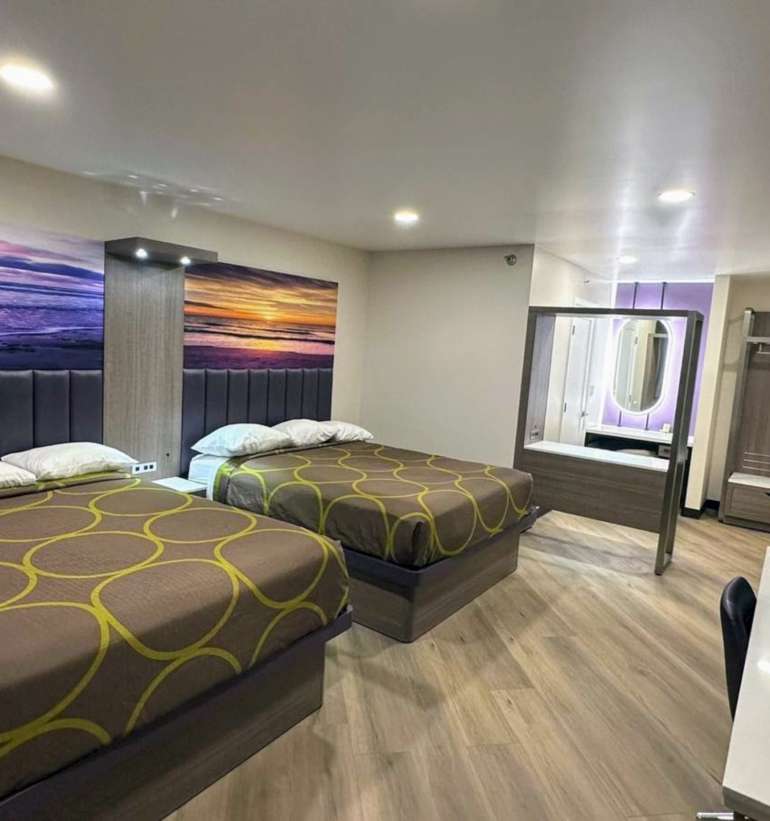 The image shows a modern hotel room with two double beds, a desk, and a mirror, featuring a beach-themed wall art.