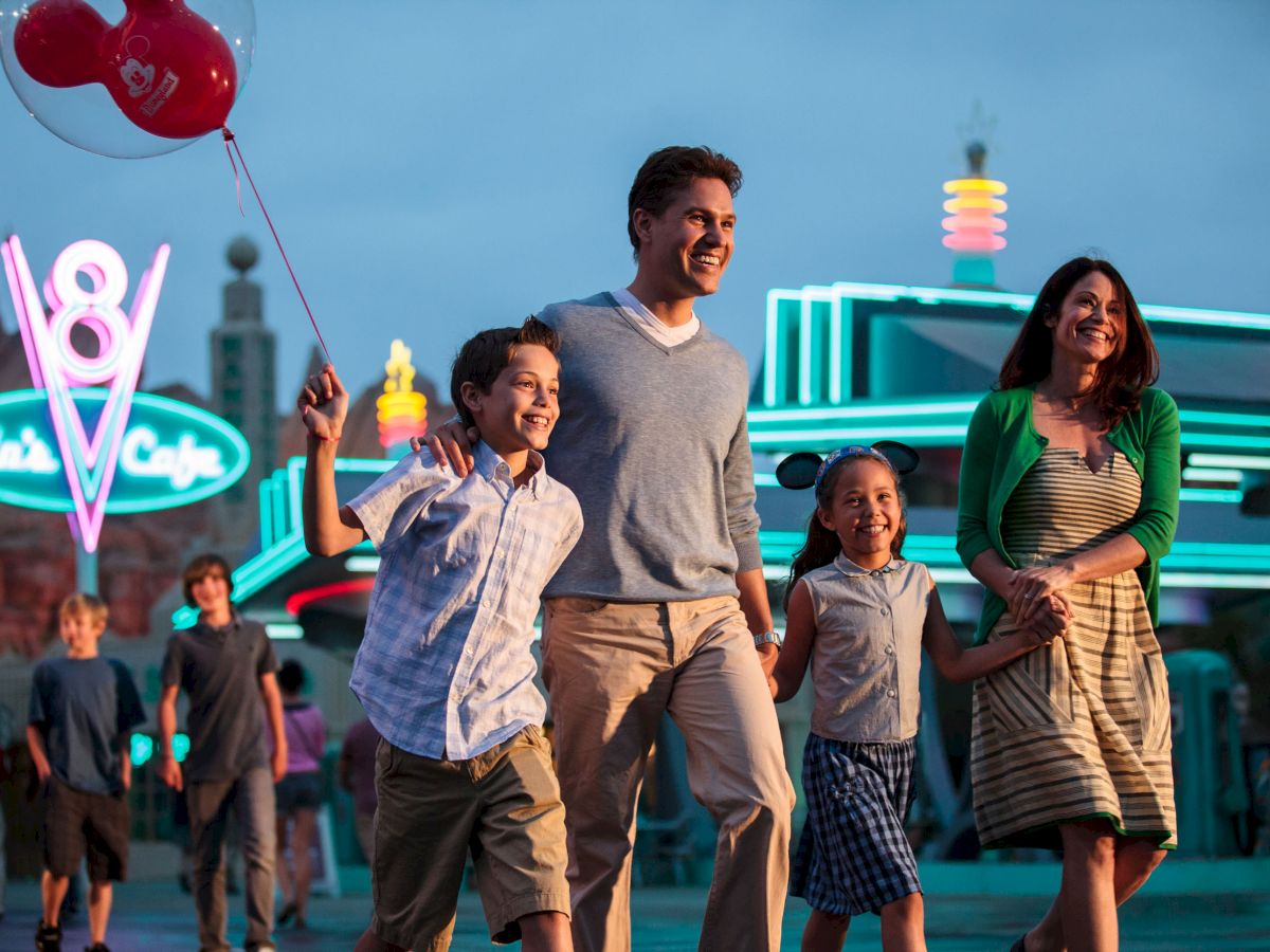 A family of four is happily walking together at an amusement park, with a diner and colorful neon lights in the background.