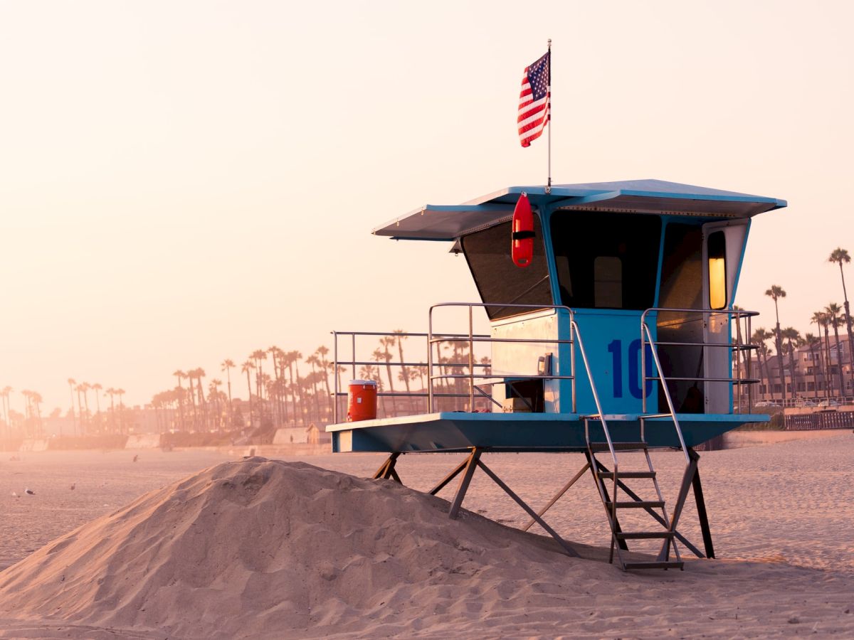 The image shows a lifeguard tower on a beach, with an American flag on top and a lifebuoy hanging on the side.