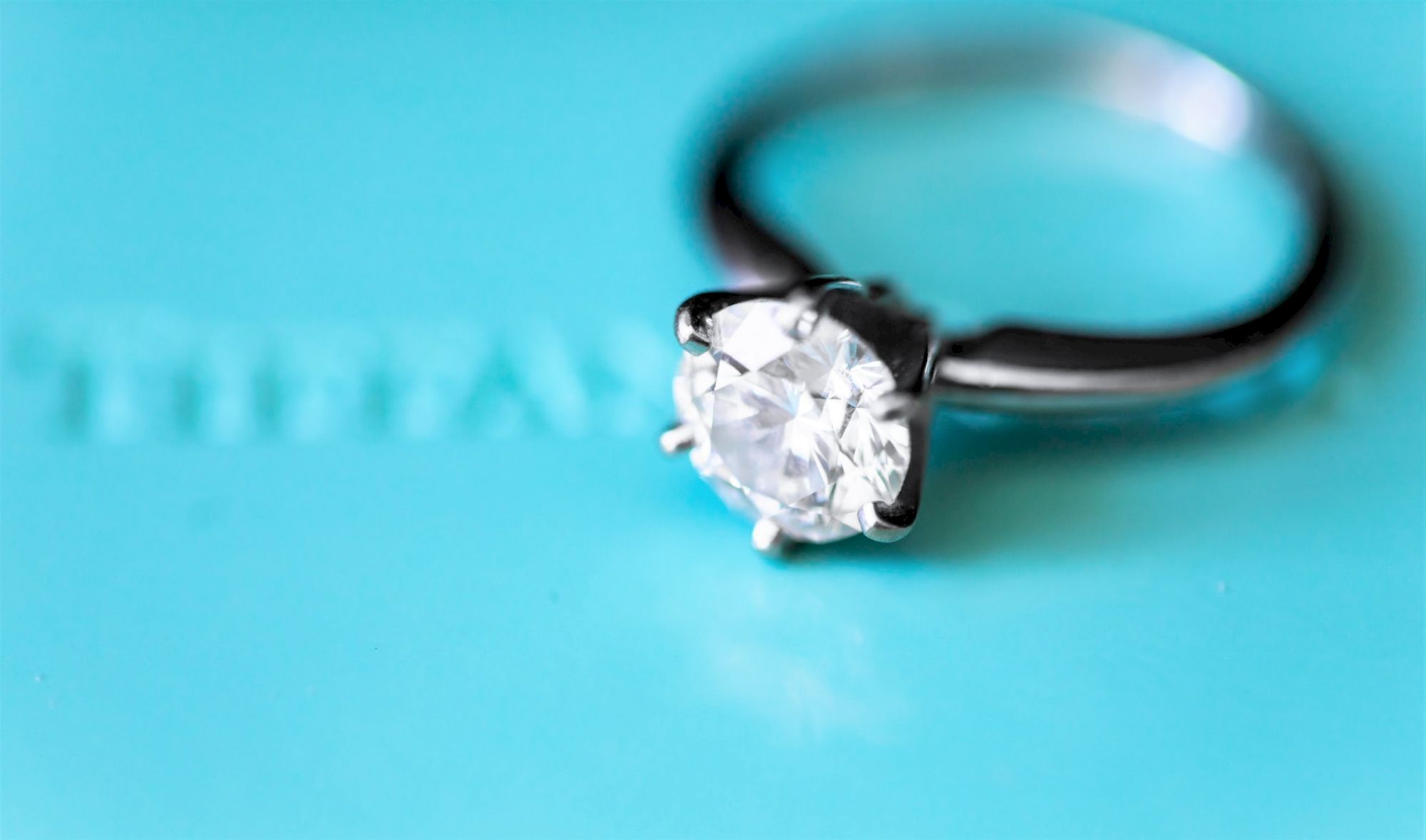 A close-up image of a diamond engagement ring on a blue background with 