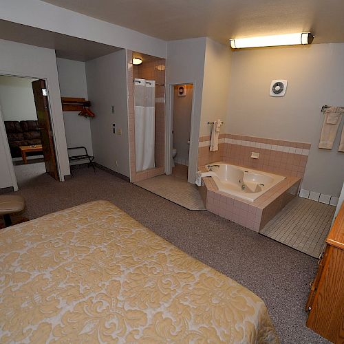 A hotel room with a bed, television, armchair, and an en-suite bathroom featuring a bathtub and shower. Towels hang on the wall.