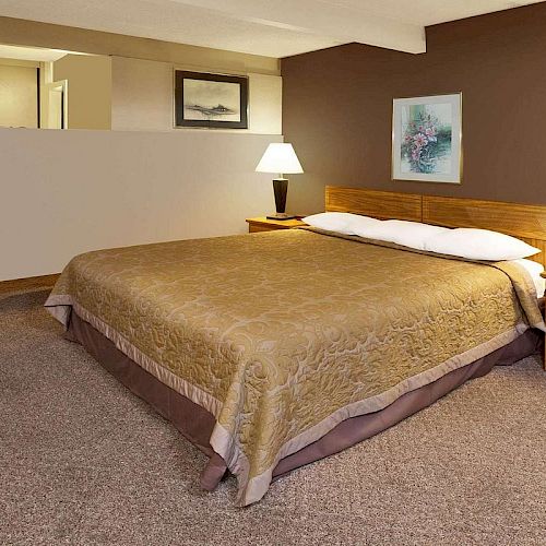 A neatly made bed in a hotel room, featuring two bedside tables with lamps, wall art, a brown accent wall, and carpet flooring, creating a cozy atmosphere.