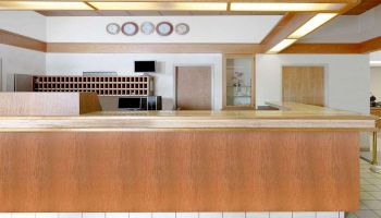 The image shows a hotel reception area with a wooden counter, clocks on the wall, and a key rack in the background ending the sentence.