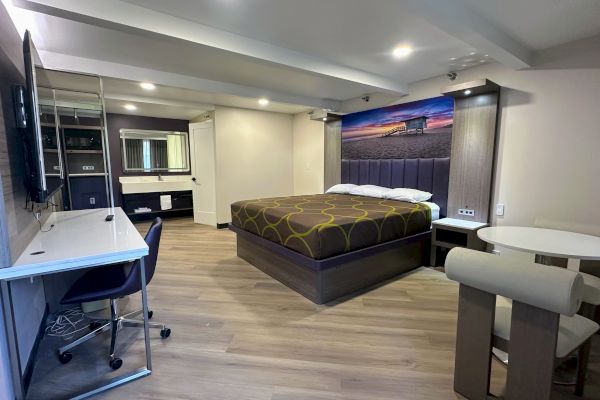 A modern hotel room with a bed, desk, chair, wall art, and small dining table. Neutral colors and minimalist design.