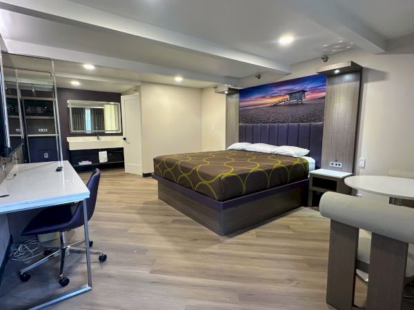A modern hotel room with a bed, desk, chair, wall art, and small dining table. Neutral colors and minimalist design.