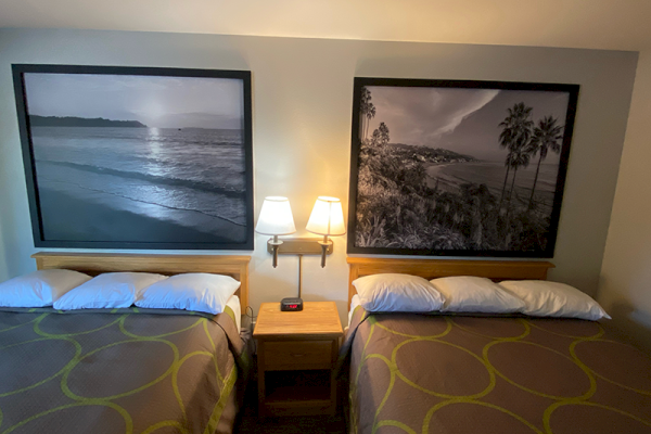 The image shows a hotel room with two double beds, a nightstand with a lamp between them, and large black-and-white beach-themed photos above each bed.