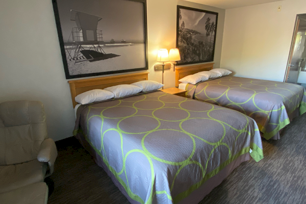 The image shows a hotel room with two double beds, a recliner chair, and framed black and white beach photos above the beds, ending the sentence.