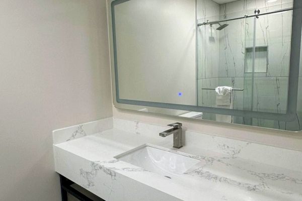 A modern bathroom with a marble sink, large mirror, and patterned floor tiles. A towel hangs below the sink.