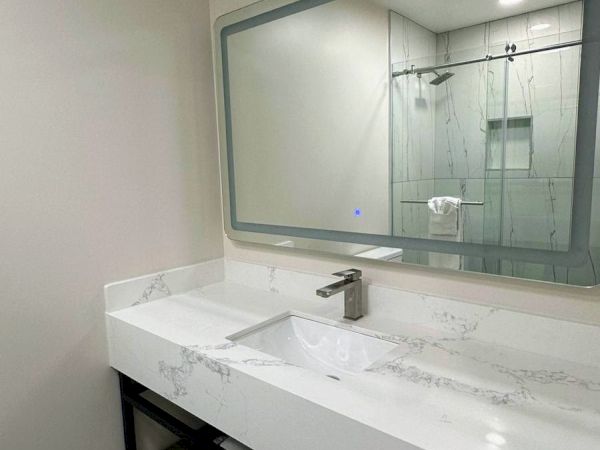 A modern bathroom with a marble sink, large mirror, and patterned floor tiles. A towel hangs below the sink.
