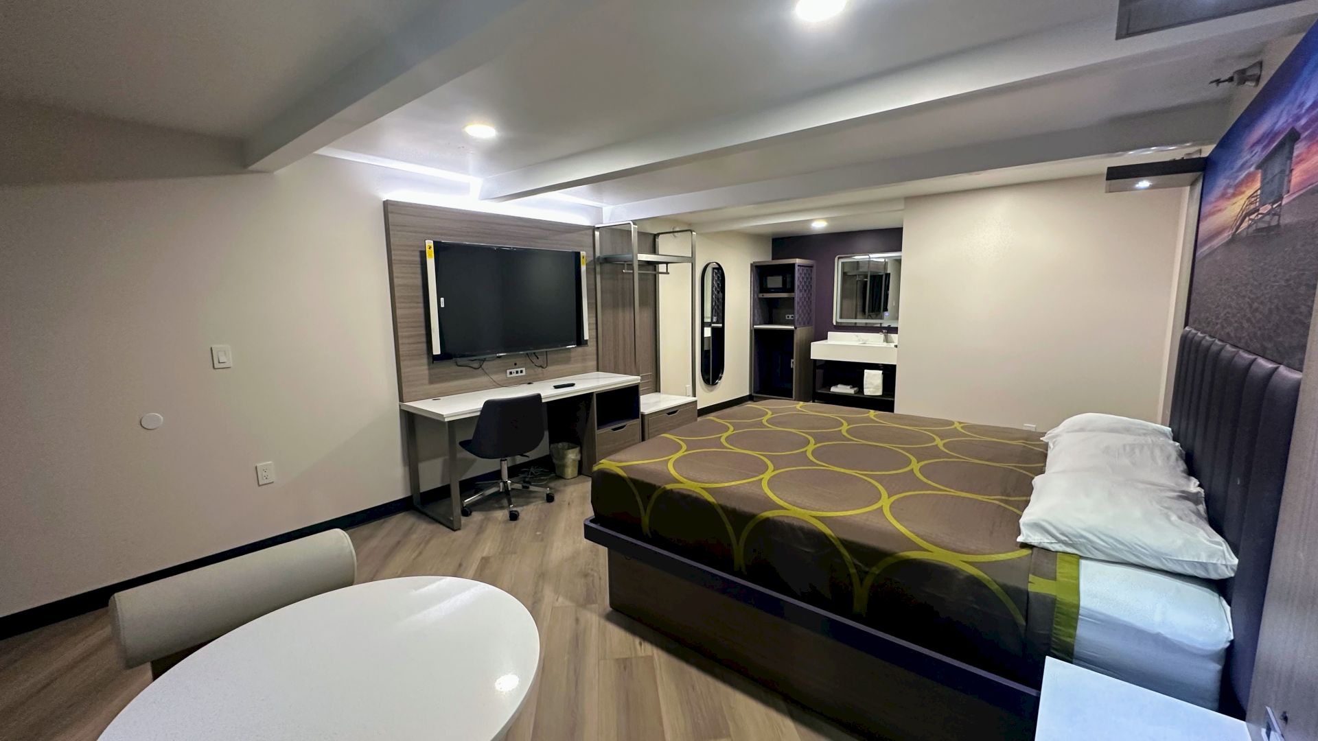 A modern hotel room with a bed, desk, TV, and seating area, featuring contemporary design and lighting.