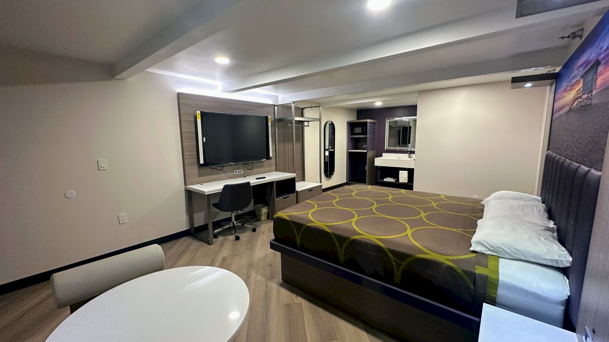 A modern hotel room with a bed, desk, TV, and seating area, featuring contemporary design and lighting.